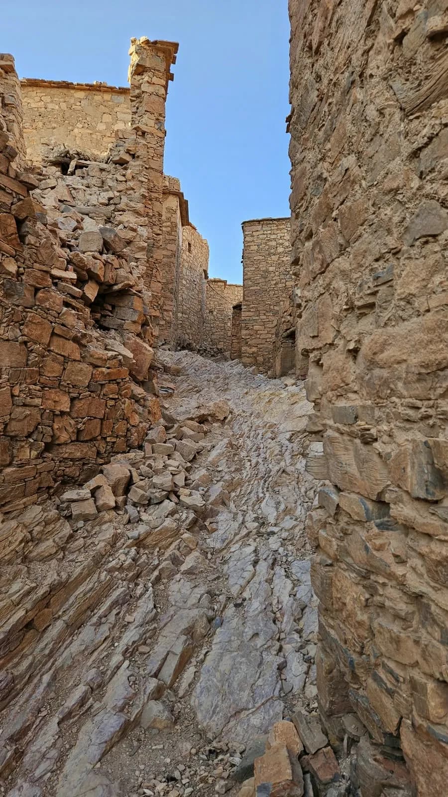 زقاق يصعد فوق الصخر العاري بين البيوت الحجرية، تحت السماء الزرقاء.