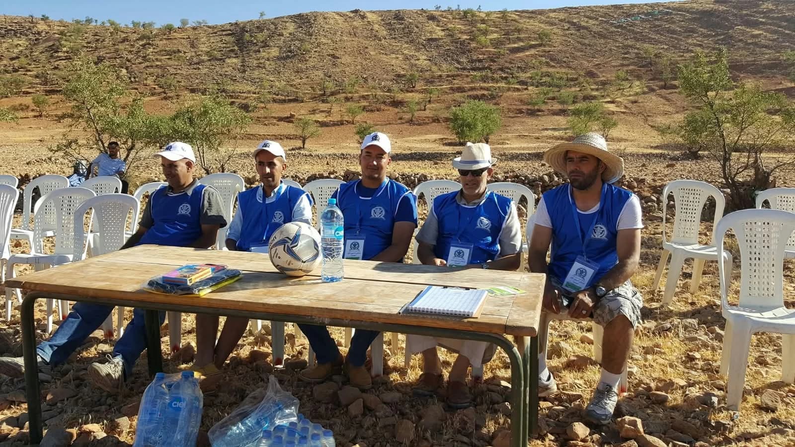 Cinq membres du comité d'organisation, en gilet bleu, assis à la table du tournoi au bord du terrain.