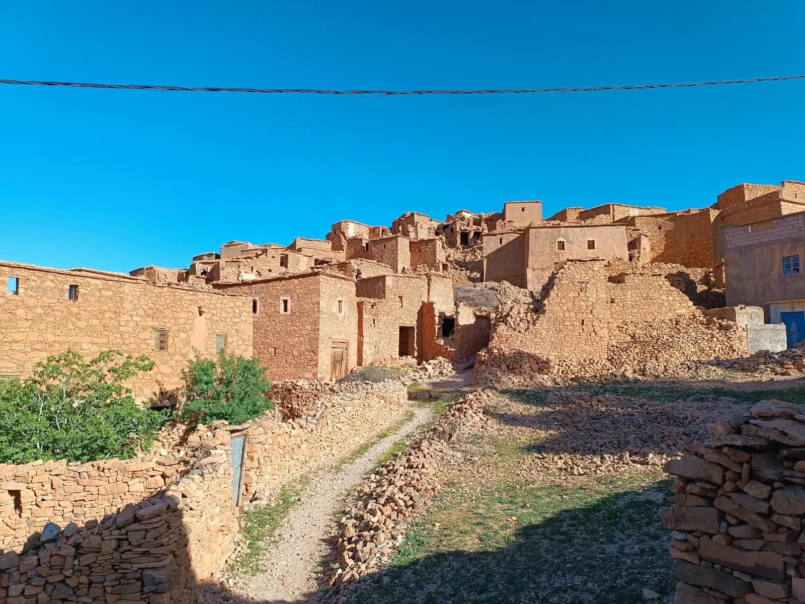 بيوت الدوار القديم من الحجر، بعضها متهدّم، وممرّ بين الجدران الحجرية تحت سماء زرقاء.
